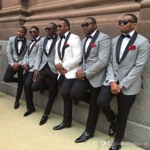 men on suit with groom at the center leaning on the wall with one leg up - amazepaperie